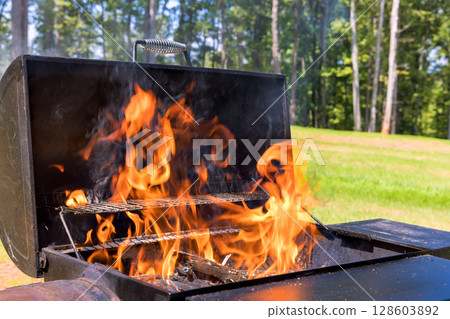 Flames dance from barbecue grill as summer sun shines down in green backyard. 128603892