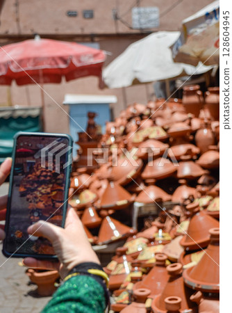 Hand with a mobile phone taking a photo of a set of tagines displayed in street Hand with a mobile phone taking a photo of a set of tagines displayed in street 128604945