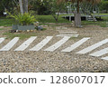 A natural garden path of light planks on gravel, surrounded by green grass, trees, and potted plants, leading towards a geodesic dome structure in the background. Peaceful park landscape. 128607017