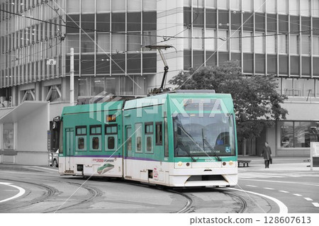 [Partially edited, blurred driver logo] Hakodate City Tram passing through the curve in front of Hakodate Station 128607613