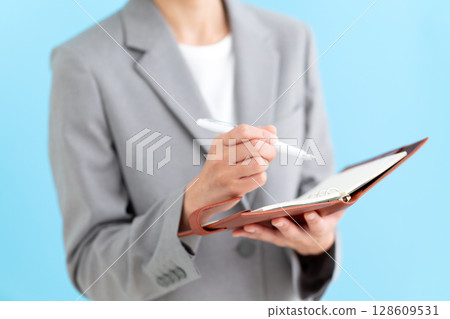 A middle-aged female business woman wearing a suit and holding a notebook A middle-aged female business woman wearing a suit and holding a notebook 128609531