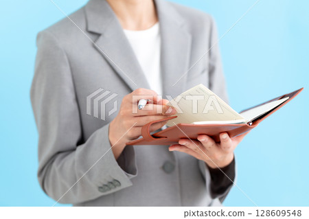 A middle-aged female business woman wearing a suit and holding a notebook A middle-aged female business woman wearing a suit and holding a notebook 128609548