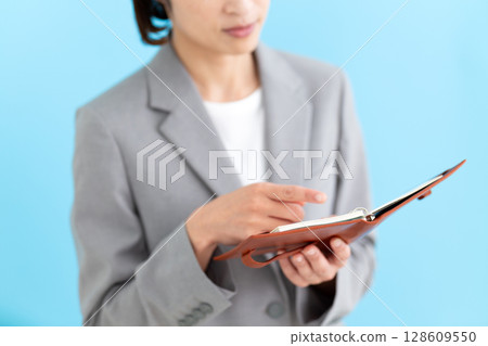A middle-aged female business woman wearing a suit and holding a notebook 128609550