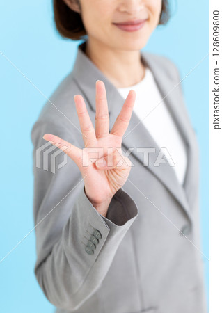 A middle-aged female business woman wearing a gray suit and holding up four fingers A middle-aged female business woman wearing a gray suit and holding up four fingers 128609800