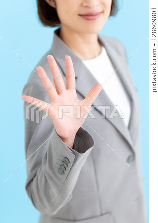 A middle-aged female business woman wearing a gray suit and holding up five fingers A middle-aged female business woman wearing a gray suit and holding up five fingers 128609801