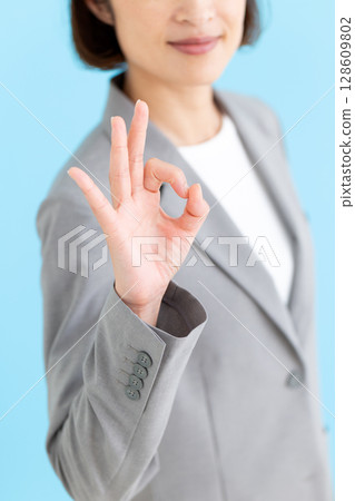 A middle-aged female business woman wearing a gray suit making a circle sign 128609802