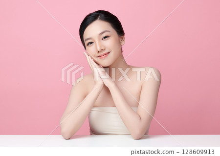 A beautiful young Asian woman with clean, fresh skin against a pink background. Skincare, facial treatment, cosmetology, beauty, and spa. An elegant portrait of an Asian woman. A beautiful young Asian woman with clean, fresh skin against a pink background. Skincare, facial treatment, cosmetology, beauty, and spa. An elegant portrait of an Asian woman. 128609913