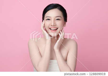 A beautiful young Asian woman with clean, fresh skin against a pink background. Skincare, facial treatment, cosmetology, beauty, and spa. An elegant portrait of an Asian woman. A beautiful young Asian woman with clean, fresh skin against a pink background. Skincare, facial treatment, cosmetology, beauty, and spa. An elegant portrait of an Asian woman. 128609919