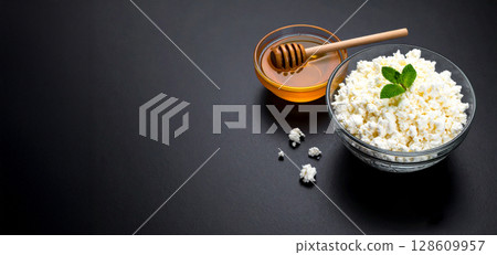 Cottage cheese and honey in a glass bowl. Black background and copy space 128609957