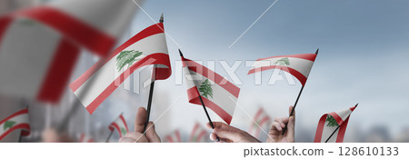 Lebanon flags in their hands on a blurred urban background Lebanon flags in their hands on a blurred urban background 128610133