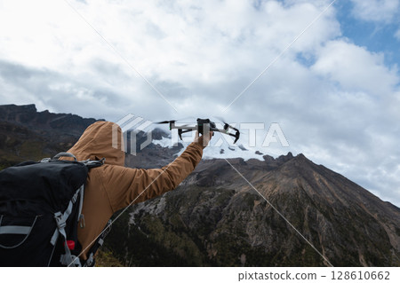 Photographer taking photo of snow capped mountain with a drone on high altitude grassland mountain top 128610662