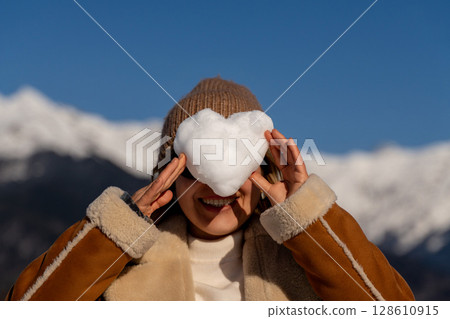 Snow Heart Woman Mountains: Winter fun, playful snow heart covering woman's eyes, joyful outdoor snowy scene. Snow Heart Woman Mountains: Winter fun, playful snow heart covering woman's eyes, joyful outdoor snowy scene. 128610915