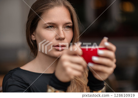 Woman Coffee Cafe: Girl holds red cup, likely coffee, at a cafe possibly for a morning drink. 128610919