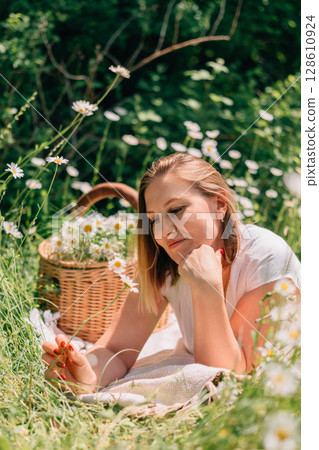 Daisies Basket Woman: Girl rests in summer field on blanket with daisies basket for a relaxing picnic. Daisies Basket Woman: Girl rests in summer field on blanket with daisies basket for a relaxing picnic. 128610924