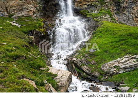 Majestic Waterfall Cascading Down Mountainside in Verdant Alpine Landscape. Tranquil Scene 128611099
