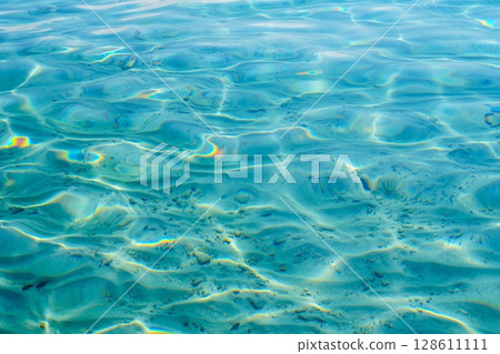 Crystal Clear Turquoise Water Surface with Sun Reflections and Sandy Seabed Texture 128611111
