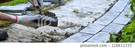 Laying paving stones on cement mortar. Laying a garden path made of tiles. Self-laying of concrete paving slabs in the courtyard of the house. do it yourself. DIY 128611155