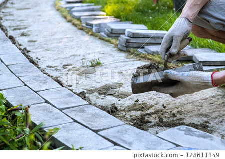 Laying paving stones on cement mortar. Laying a garden path made of tiles. Self-laying of concrete paving slabs in the courtyard of the house. do it yourself. DIY 128611159
