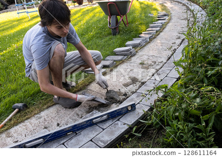 Laying paving stones on cement mortar. Laying a garden path made of tiles. Self-laying of concrete paving slabs in the courtyard of the house. do it yourself. DIY Laying paving stones on cement mortar. Laying a garden path made of tiles. Self-laying of concrete paving slabs in the courtyard of the house. do it yourself. DIY 128611164