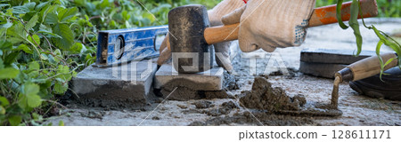 Laying paving stones on cement mortar. banner. Laying a garden path made of tiles. Self-laying of concrete paving slabs in the courtyard of the house. do it yourself. DIY 128611171