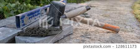 Laying paving stones on cement mortar. banner, Laying a garden path made of tiles. Self-laying of concrete paving slabs in the courtyard of the house. do it yourself. DIY 128611173