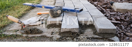Banner. Laying paving stones on cement mortar. Laying a garden path made of tiles. Self-laying of concrete paving slabs in the courtyard of the house. do it yourself. DIY Banner. Laying paving stones on cement mortar. Laying a garden path made of tiles. Self-laying of concrete paving slabs in the courtyard of the house. do it yourself. DIY 128611177
