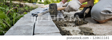 Laying paving stones on cement mortar. Banner. Laying a garden path made of tiles. Self-laying of concrete paving slabs in the courtyard of the house. do it yourself. DIY 128611181