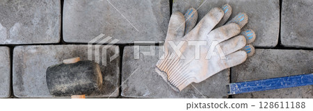 Laying paving stones on cement mortar. Banner. Gloves. Laying a garden path made of tiles. Self-laying of concrete paving slabs in the courtyard of the house. do it yourself. DIY Laying paving stones on cement mortar. Banner. Gloves. Laying a garden path made of tiles. Self-laying of concrete paving slabs in the courtyard of the house. do it yourself. DIY 128611188
