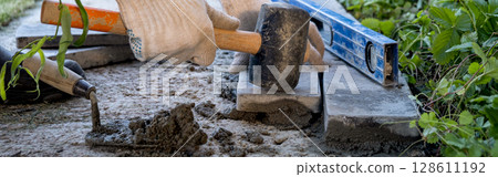 banner. Laying paving stones on cement mortar. Laying a garden path made of tiles. Self-laying of concrete paving slabs in the courtyard of the house. do it yourself. DIY banner. Laying paving stones on cement mortar. Laying a garden path made of tiles. Self-laying of concrete paving slabs in the courtyard of the house. do it yourself. DIY 128611192