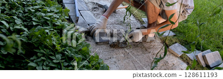 Laying paving stones on cement mortar. banner, Laying a garden path made of tiles. Self-laying of concrete paving slabs in the courtyard of the house. do it yourself. DIY 128611193