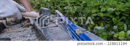 Laying paving stones on cement mortar. Laying a garden path made of tiles. Self-laying of concrete paving slabs in the courtyard of the house. do it yourself. DIY Laying paving stones on cement mortar. Laying a garden path made of tiles. Self-laying of concrete paving slabs in the courtyard of the house. do it yourself. DIY 128611194