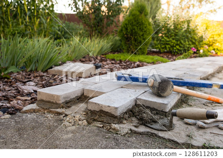 Laying paving stones on cement mortar. Laying a garden path made of tiles. Self-laying of concrete paving slabs in the courtyard of the house. do it yourself. DIY Laying paving stones on cement mortar. Laying a garden path made of tiles. Self-laying of concrete paving slabs in the courtyard of the house. do it yourself. DIY 128611203