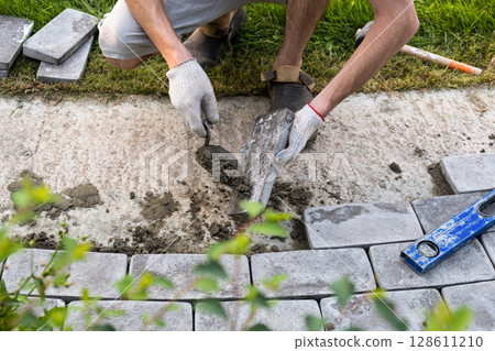 Laying paving stones on cement mortar. Laying a garden path made of tiles. Self-laying of concrete paving slabs in the courtyard of the house. do it yourself. DIY Laying paving stones on cement mortar. Laying a garden path made of tiles. Self-laying of concrete paving slabs in the courtyard of the house. do it yourself. DIY 128611210