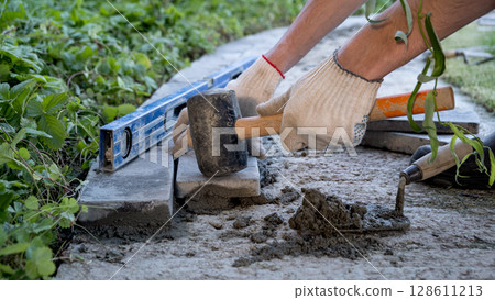 Laying paving stones on cement mortar. Laying a garden path made of tiles. Self-laying of concrete paving slabs in the courtyard of the house. do it yourself. DIY 128611213