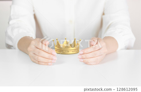 Hands Gently Holding a Gold Crown Symbolizing Leadership, Success and Royalty Protection 128612095