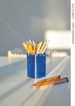 Yellow pencils in blue holder on white table with natural sunlight and shadows Yellow pencils in blue holder on white table with natural sunlight and shadows 128612143