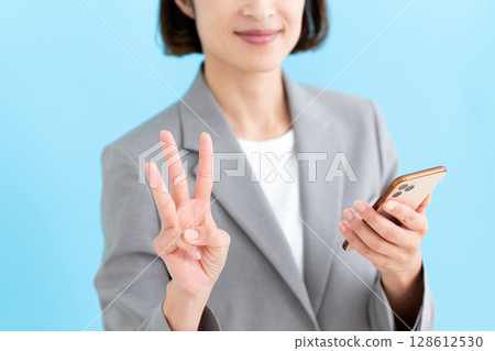 一位中年女商界女性手持智慧型手機，三根手指指向上方 128612530