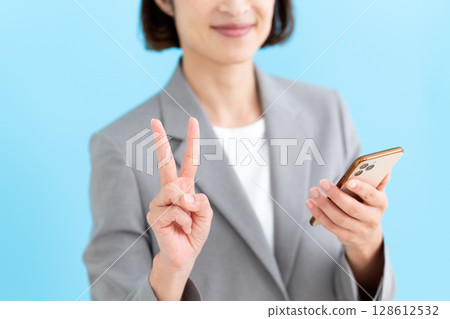 A middle-aged female business woman holding a smartphone and pointing up two fingers 128612532