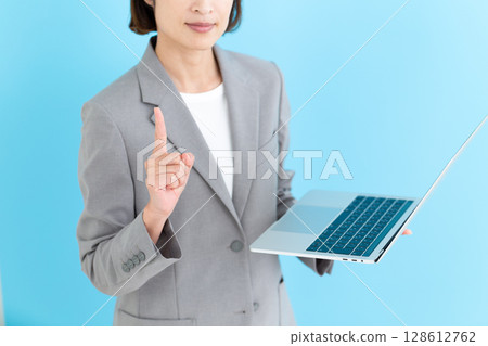 一位中年女商界女性拿著筆記型電腦,食指向上 一位中年女商界女性拿著筆記型電腦,食指向上 128612762