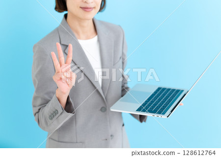 A middle-aged female business woman holding a laptop computer and pointing up three fingers 128612764