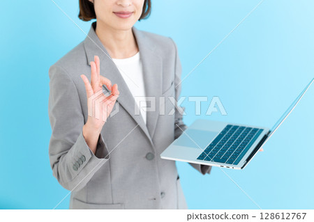 A middle-aged female business woman holding a laptop and making a circle sign 128612767