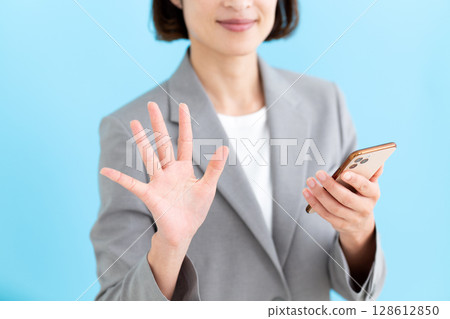 A middle-aged female business woman holding a smartphone and showing five fingers A middle-aged female business woman holding a smartphone and showing five fingers 128612850