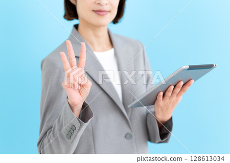 A middle-aged female business woman holding a tablet and pointing up three fingers A middle-aged female business woman holding a tablet and pointing up three fingers 128613034