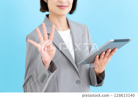 A middle-aged female business woman holding a tablet and pointing four fingers up A middle-aged female business woman holding a tablet and pointing four fingers up 128613140