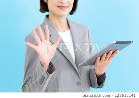 A middle-aged female business woman holding a tablet and showing five fingers A middle-aged female business woman holding a tablet and showing five fingers 128613141