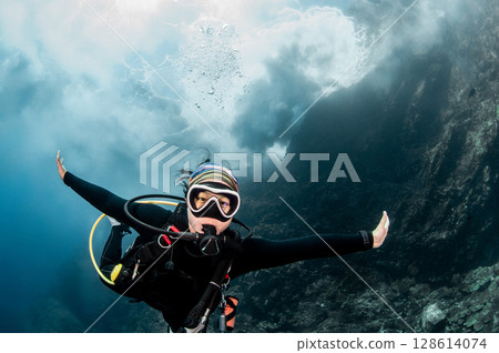 Asian female scuba diver looking at camera posing with the stunning wave breaking exploding above Asian female scuba diver looking at camera posing with the stunning wave breaking exploding above 128614074