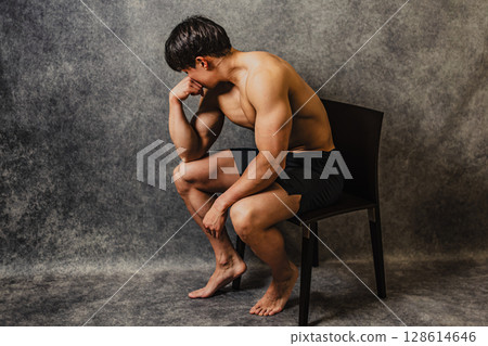 A man showing off his muscular beauty while sitting on a chair and posing as if he is thinking A man showing off his muscular beauty while sitting on a chair and posing as if he is thinking 128614646