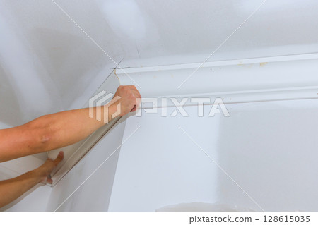 Hands work carefully to install crown molding in freshly painted room during home renovation efforts. 128615035