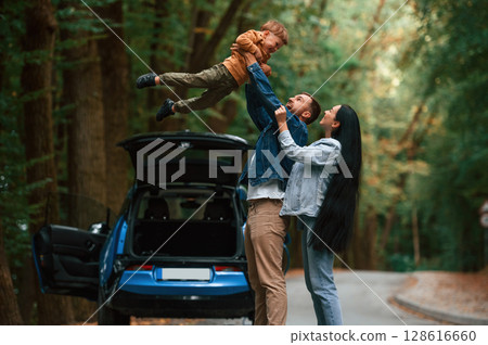 Boy in hands, happiness. Father, mother and son are having fun together near blue car outdoors 128616660