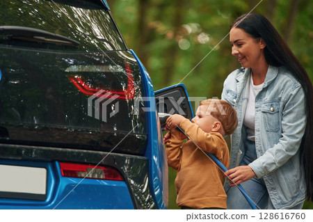 Side view. Mother with her little son are charging the electric car outdoors 128616760